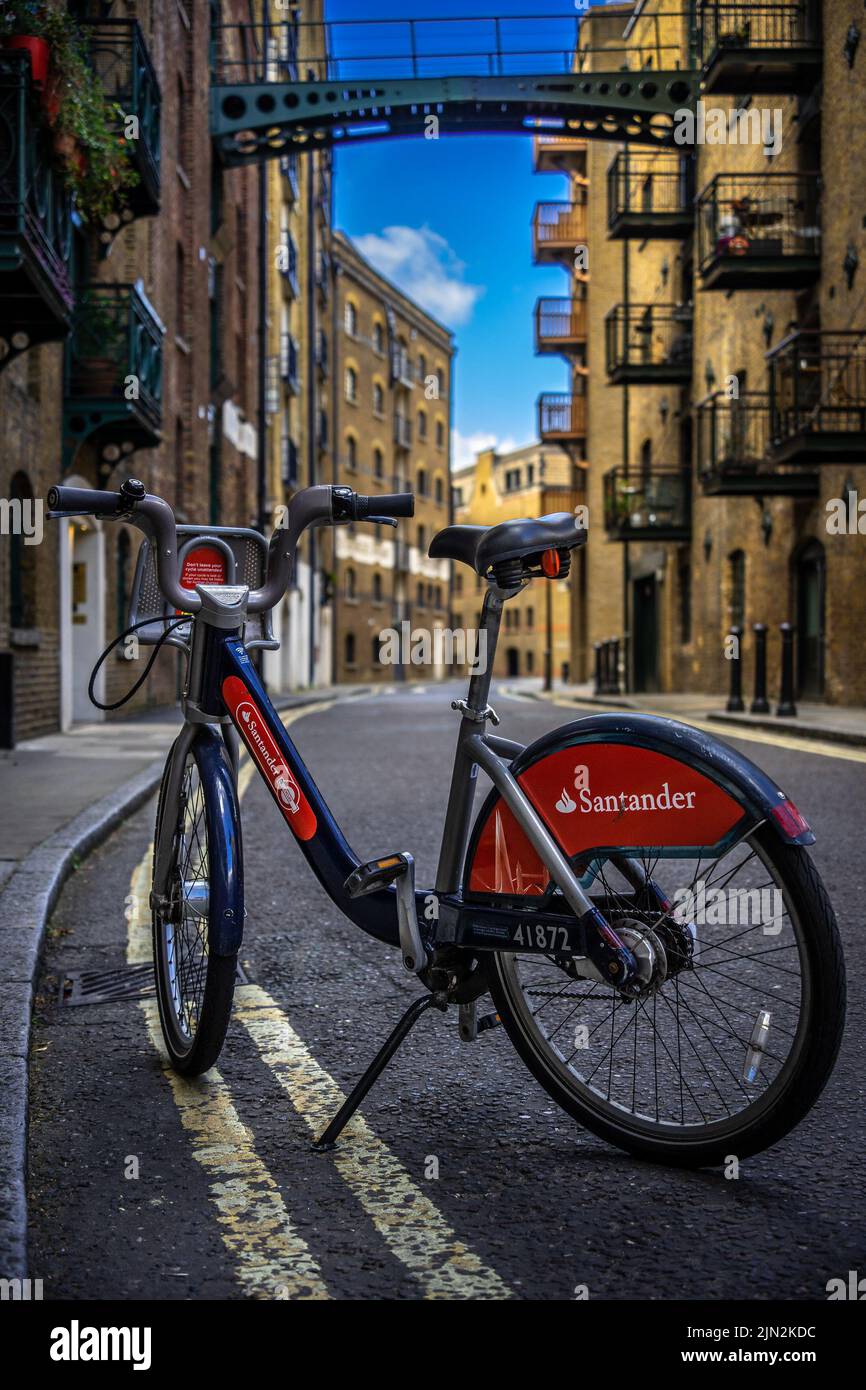 Santander Bike parking in the middle of Shad Thames, one of the oldest streets of London, with warehouses in the background; Sustainable Bike sharing Stock Photo