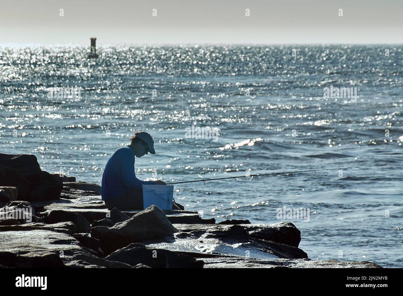 An early morning fisherman tends to his equipment on the breakwater of Indian River Inlet along the Delaware seashore. Stock Photo