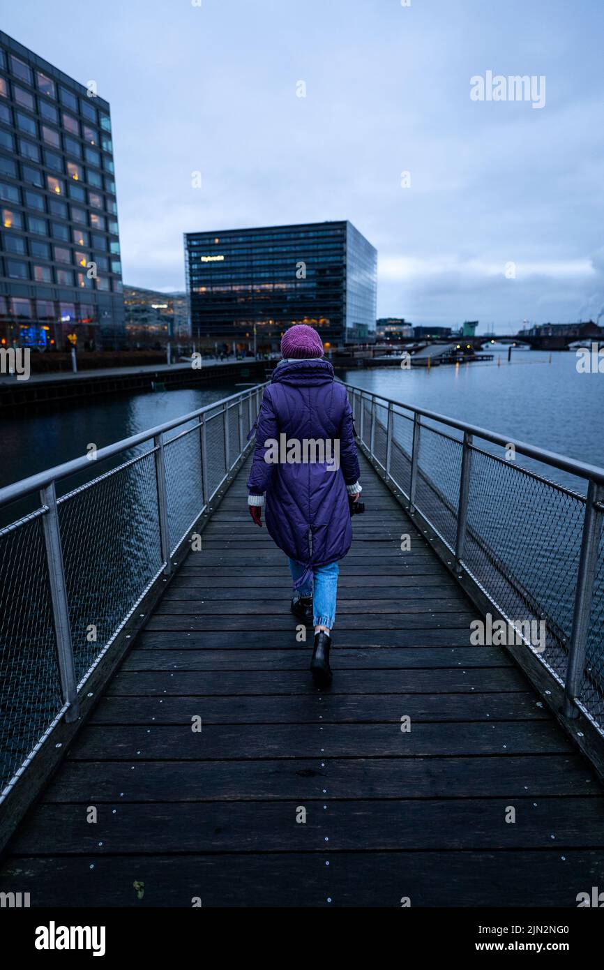 A vertical shot of a female from behind walking on a bridge in Copenhagen, Denmark Stock Photo