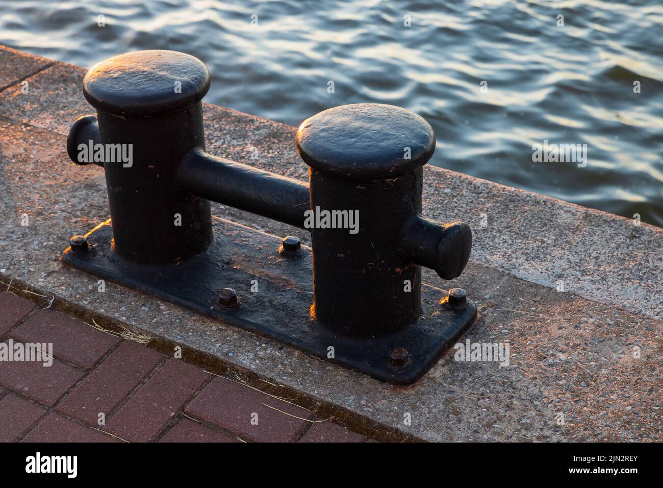 Black coastal bollard is on a concrrete pier, close up photo of port mooring equipment Stock Photo