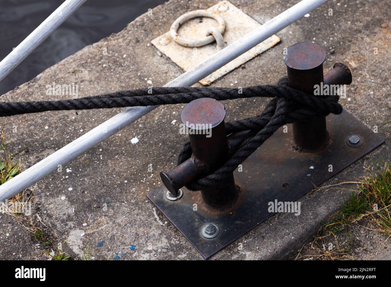 Black coastal bollard with mooring rope is on a concrrete pier ground Stock Photo