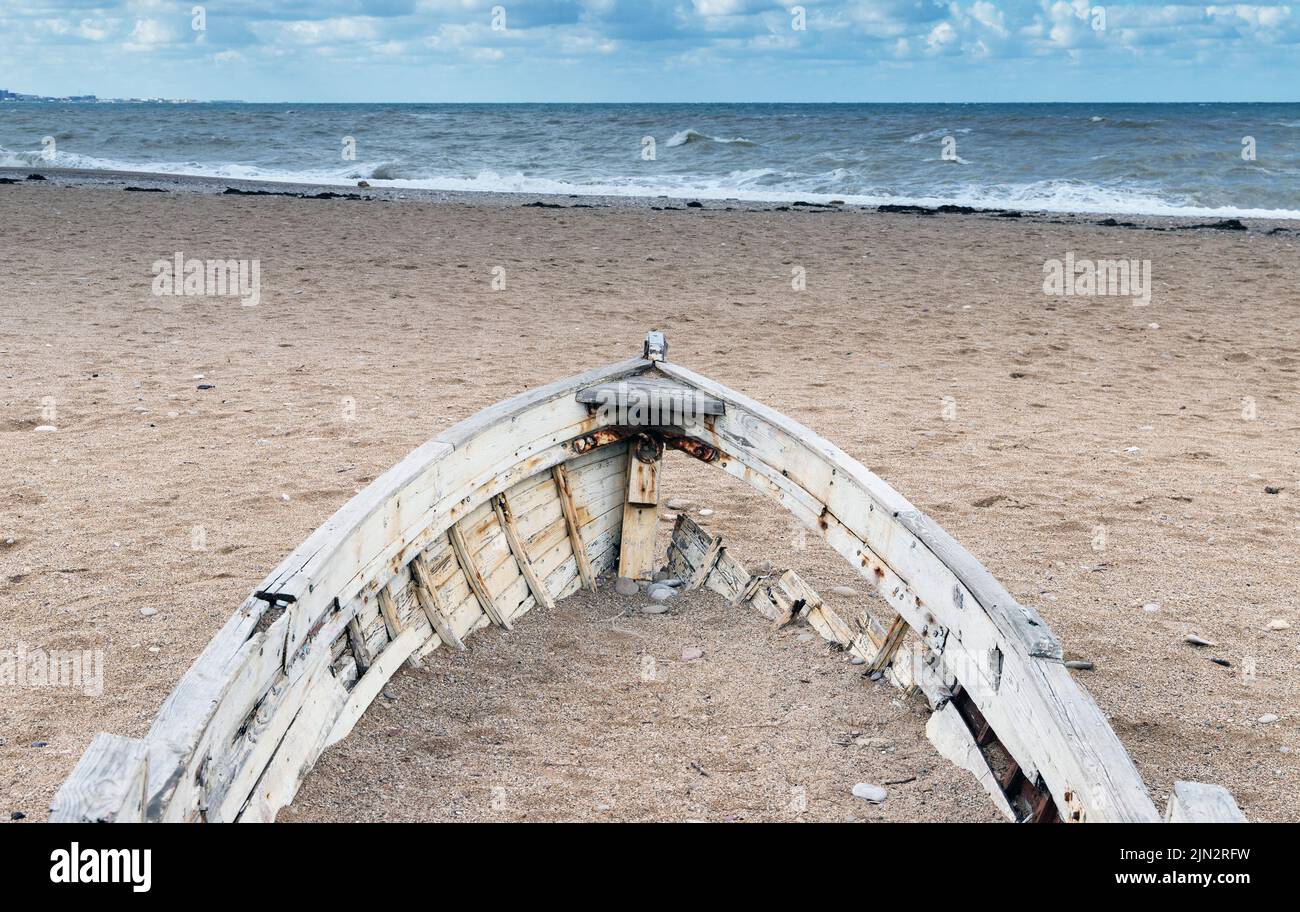 Bow of an old abandoned wooden boat laying on an empty sandy coast on a daytime Stock Photo