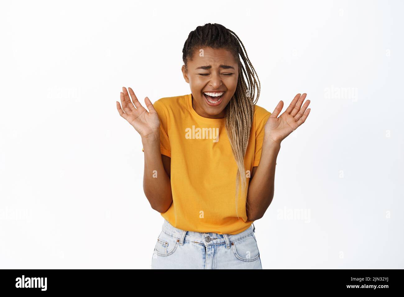 Happy, beautiful african american woman laughing and smiling, chuckle with empty hands raised up, standing in yellow tshirt over white background Stock Photo