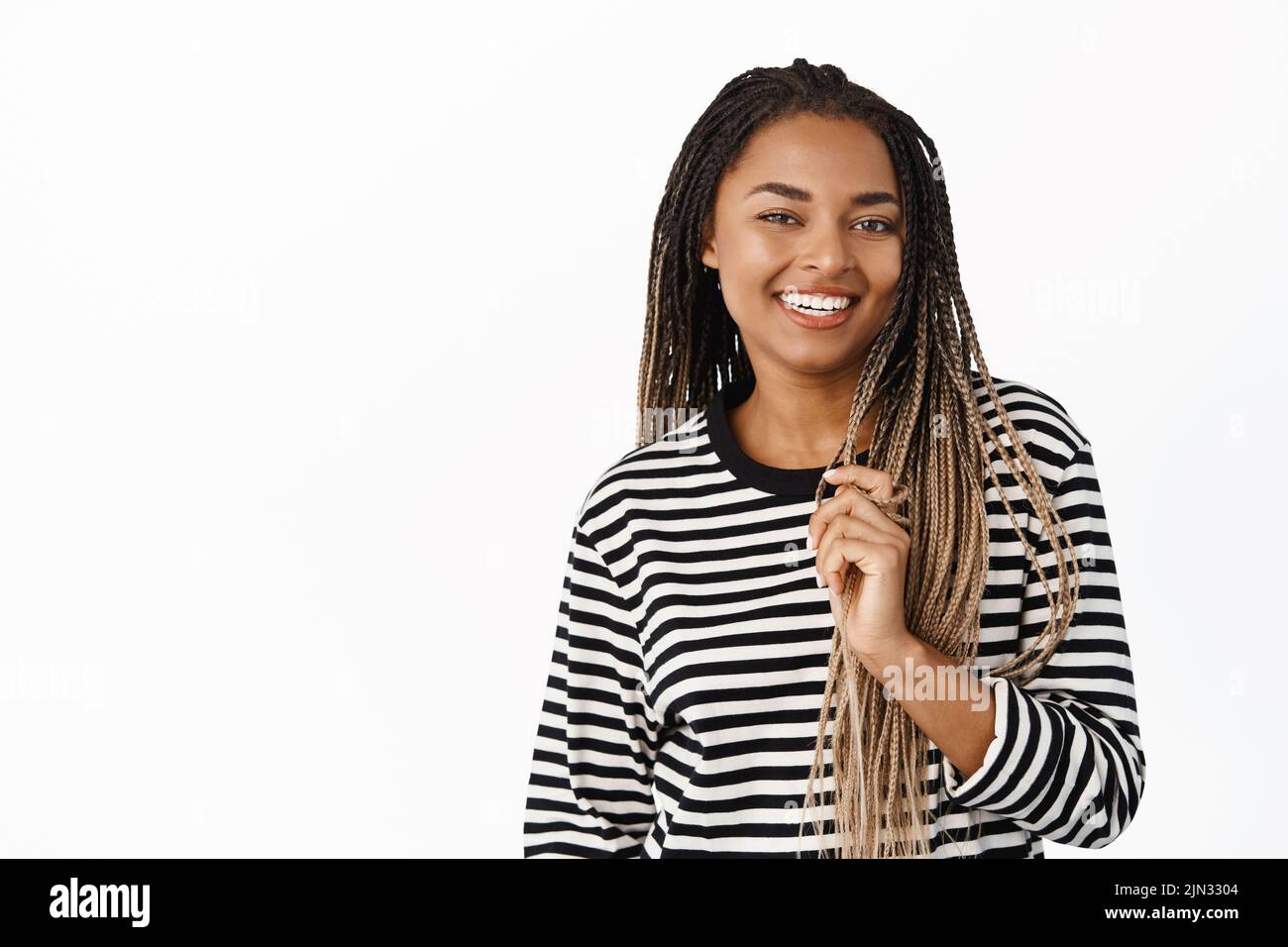 Beautiful female model with dreads, smiling and laughing, playing with braids, standing over white background Stock Photo