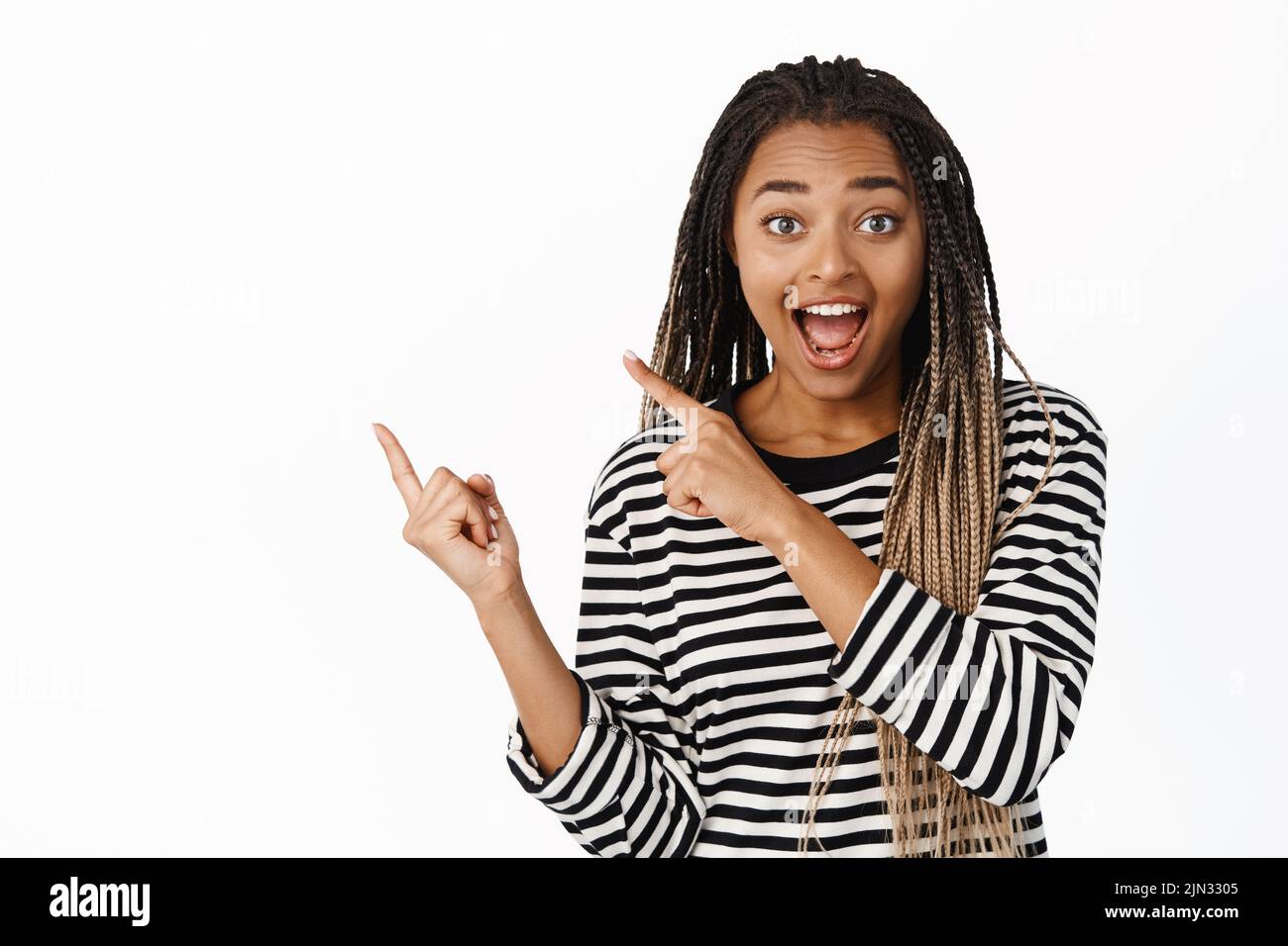 Hey check this out. Happy smiling african girl promoting, pointing left and smiling, luring people take look, showing big promo, logo on copy space Stock Photo