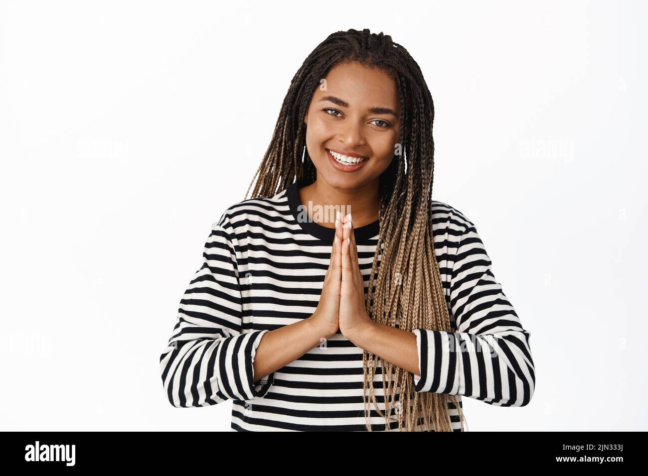 Mindfulness and meditation concept. Smiling black young woman showing namaste gesture, looking happy and relaxed, white background Stock Photo