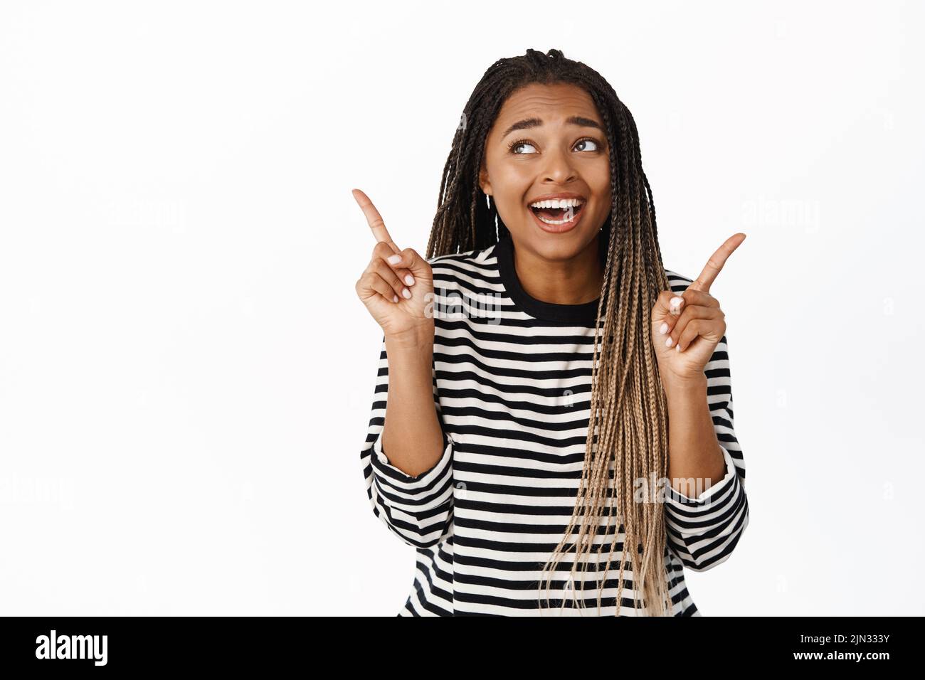 Smiling happy black girl laughing, pointing fingers at two sides, showing both variants, picking smth in store, laughing and looking at upper left Stock Photo