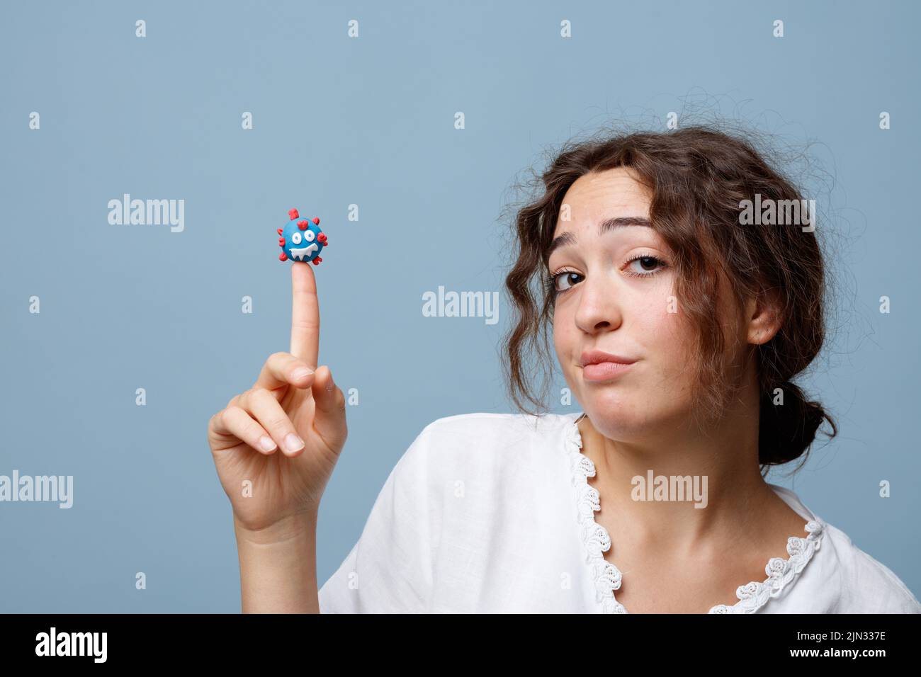 Young woman holds the puppet of a COVID-19 virus on her finger without any fear; concept of the new normal and the power of science and knowledge Stock Photo