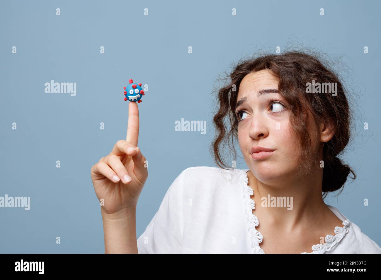 Young woman holds the puppet of a COVID-19 virus on her finger without any fear; concept of the new normal and the power of science and knowledge Stock Photo