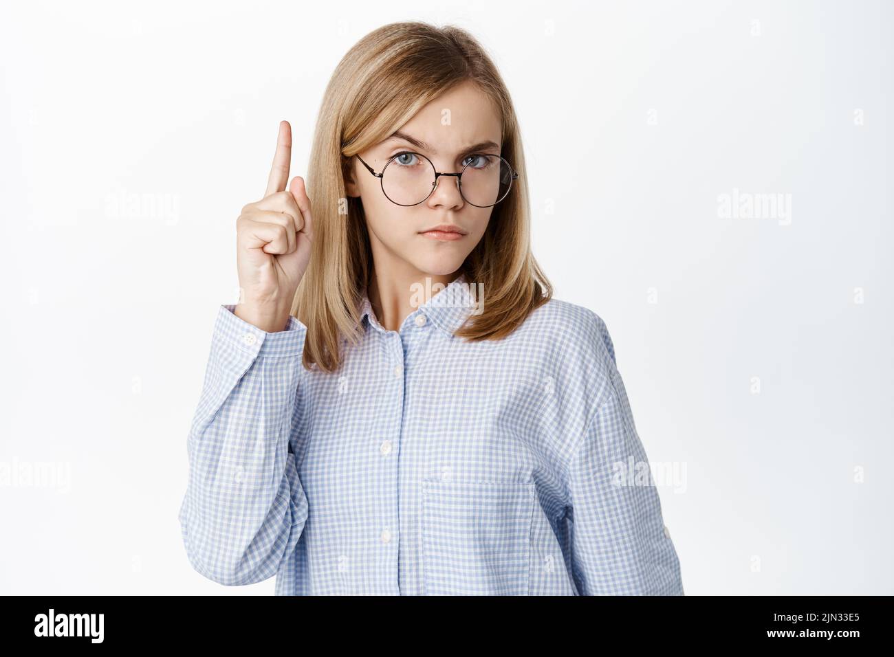 Smart cute little kid, girl in glasses raising one finger up, looking thoughtful and clever, standing over white background Stock Photo
