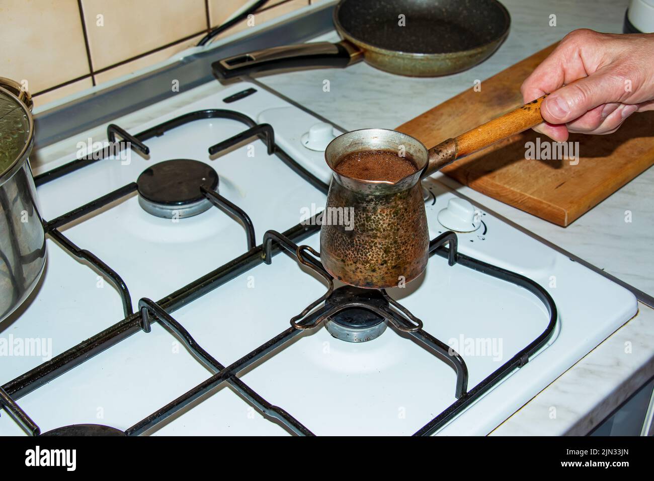 Ground coffee is brewed in a copper cezve on a gas stove. Stock Photo