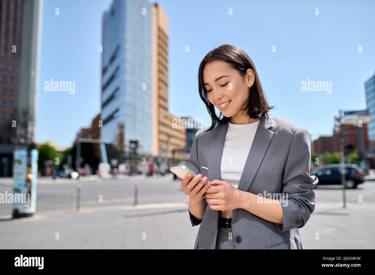 Young smiling Asian business woman using cellphone standing on city ...