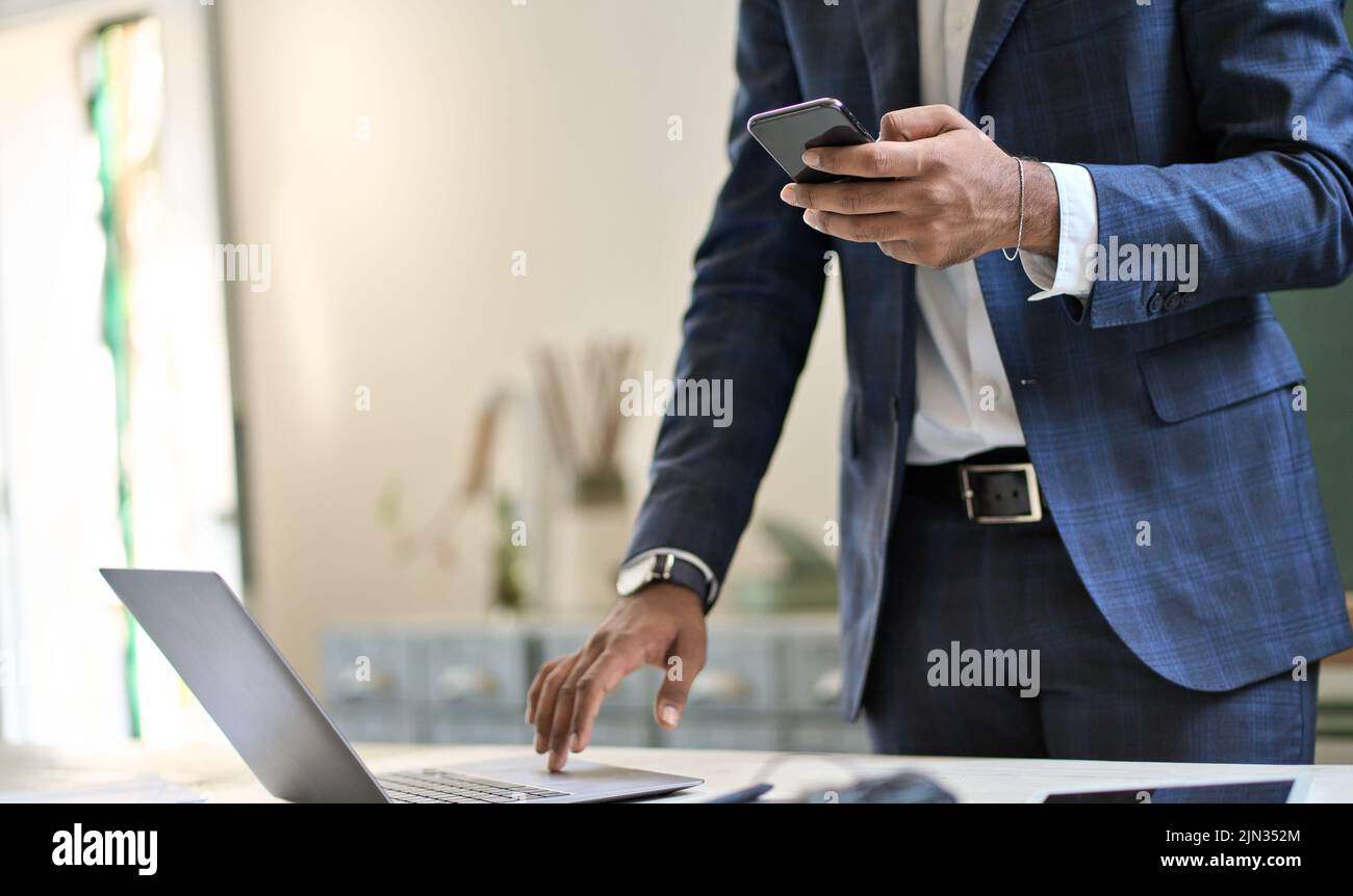 Business man wearing suit holding phone using laptop online technology. Stock Photo