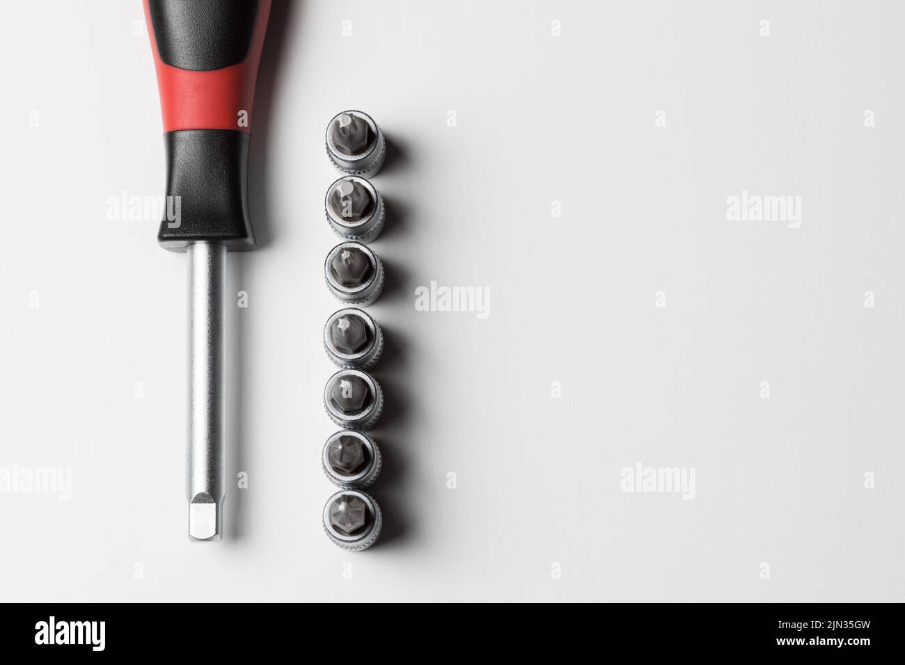 Screwdriver with attachments on the table on a white background. A set of small nozzles. View from above Stock Photo