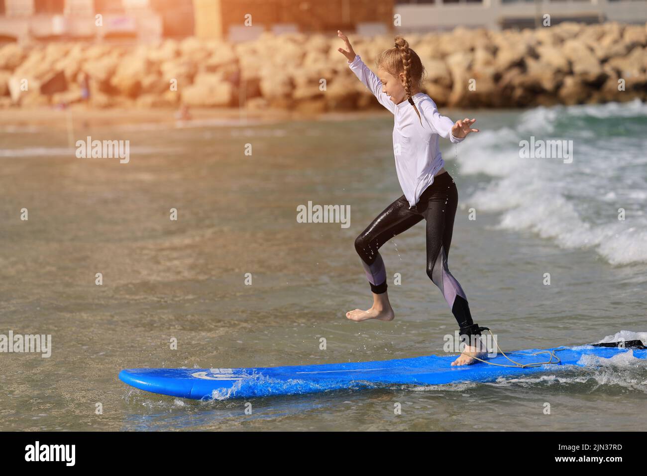 Happy baby girl young surfer ride on surfboard with fun on sea waves. Active family lifestyle, Stock Photo