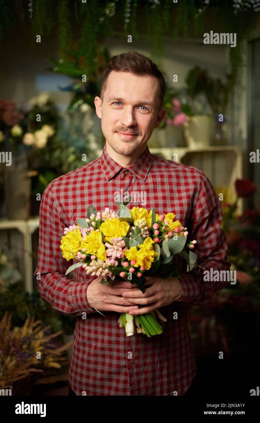 Theme of love, dating or romance concept. Attractive male in shirt holding beautiful bouquet of yellow and pink fresh flowers. Mother's Day, Valentine's Day or International Women Day holiday Stock Photo