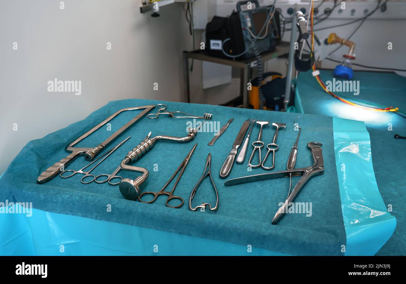 Set of steel surgical tools on blue cloth - real instruments used in mobile medical army tent, blurred operating table background Stock Photo