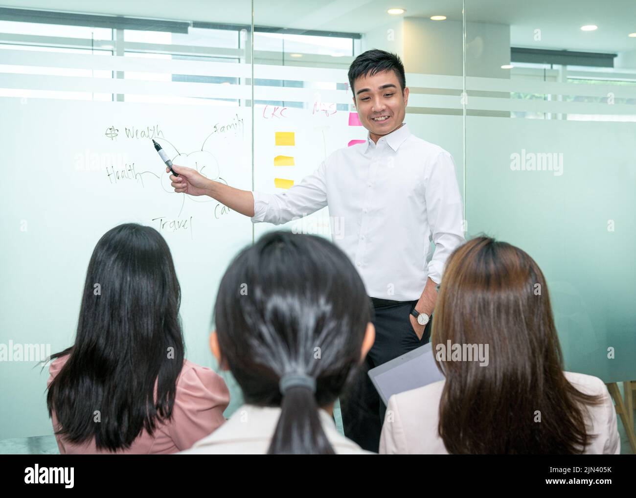 Happy looking Trainer giving a presentation on the white glass board to an audience. Stock Photo