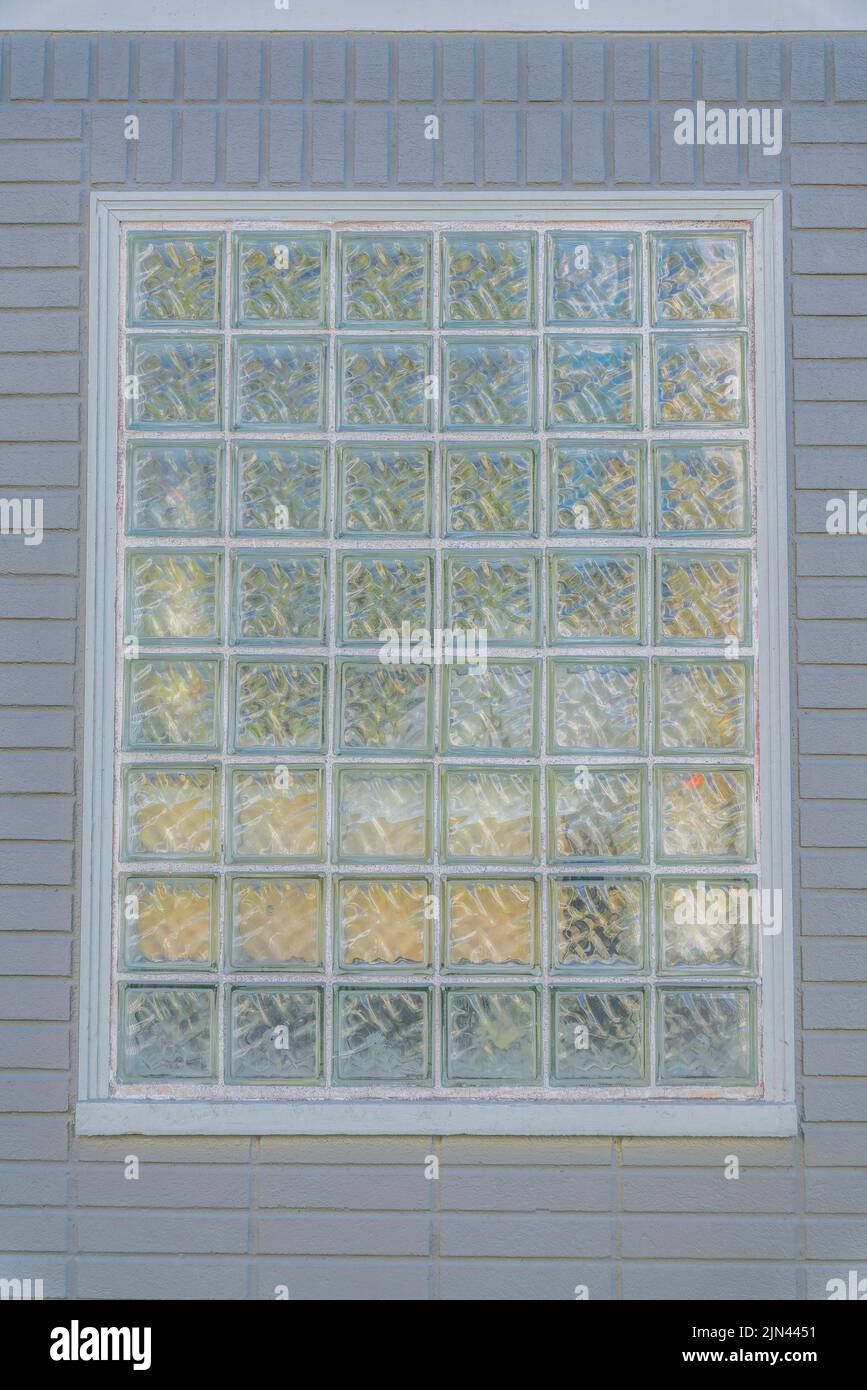 Glass blocks window at the center of a gray concrete wall with bricks