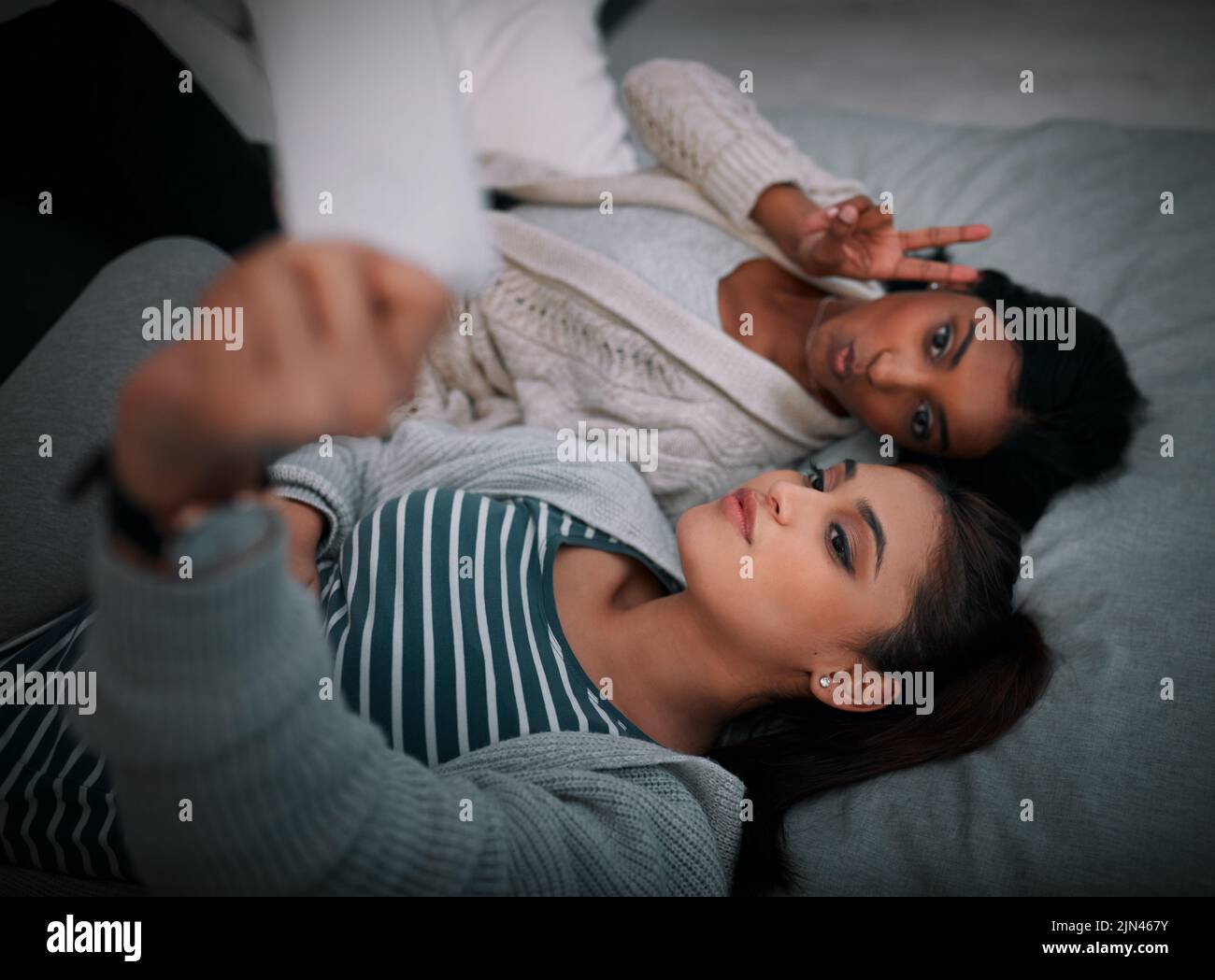 Its never too late for a selfie. two young women lying taking selfies while lying on a bed. Stock Photo