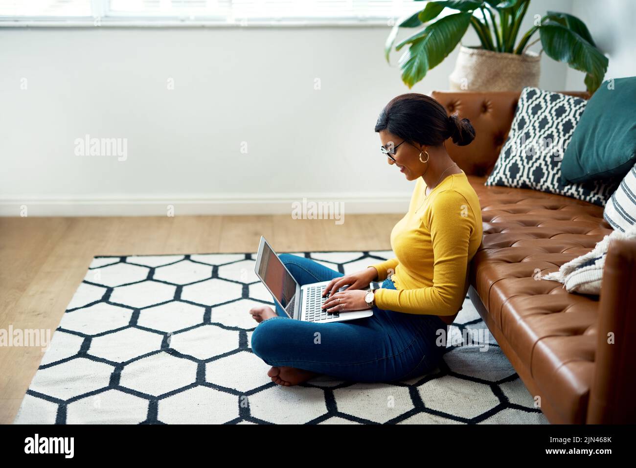 Blogging is my passion. an attractive young woman sitting crosslegged on the floor and using her laptop at home. Stock Photo