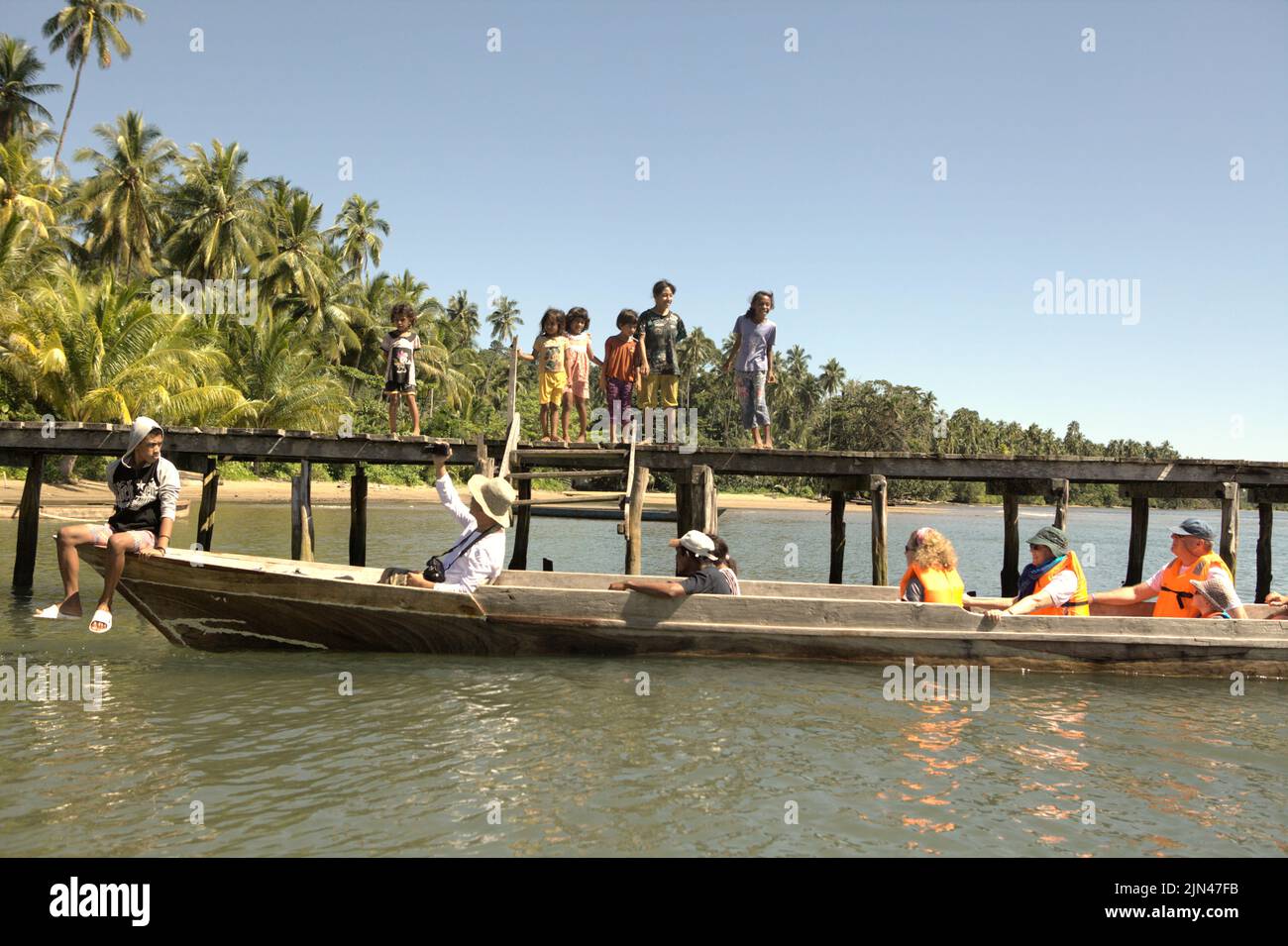 Children standing on a jetty as a boat carrying tourists is arriving Horale village in Seram Utara Barat, Maluku Tengah, Maluku, Indonesia. Stock Photo