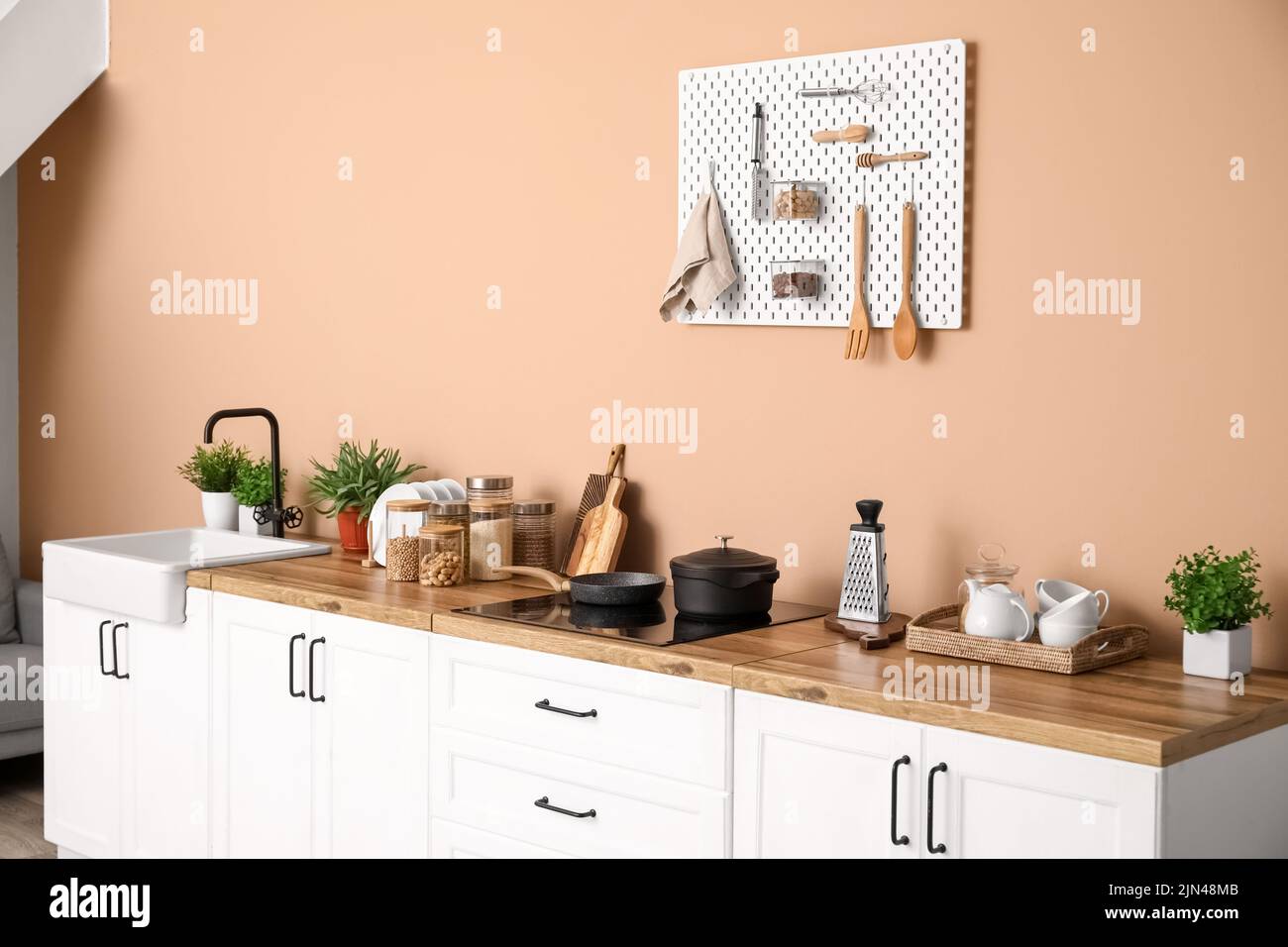 Interior of stylish kitchen with white counters, utensils and pegboard ...