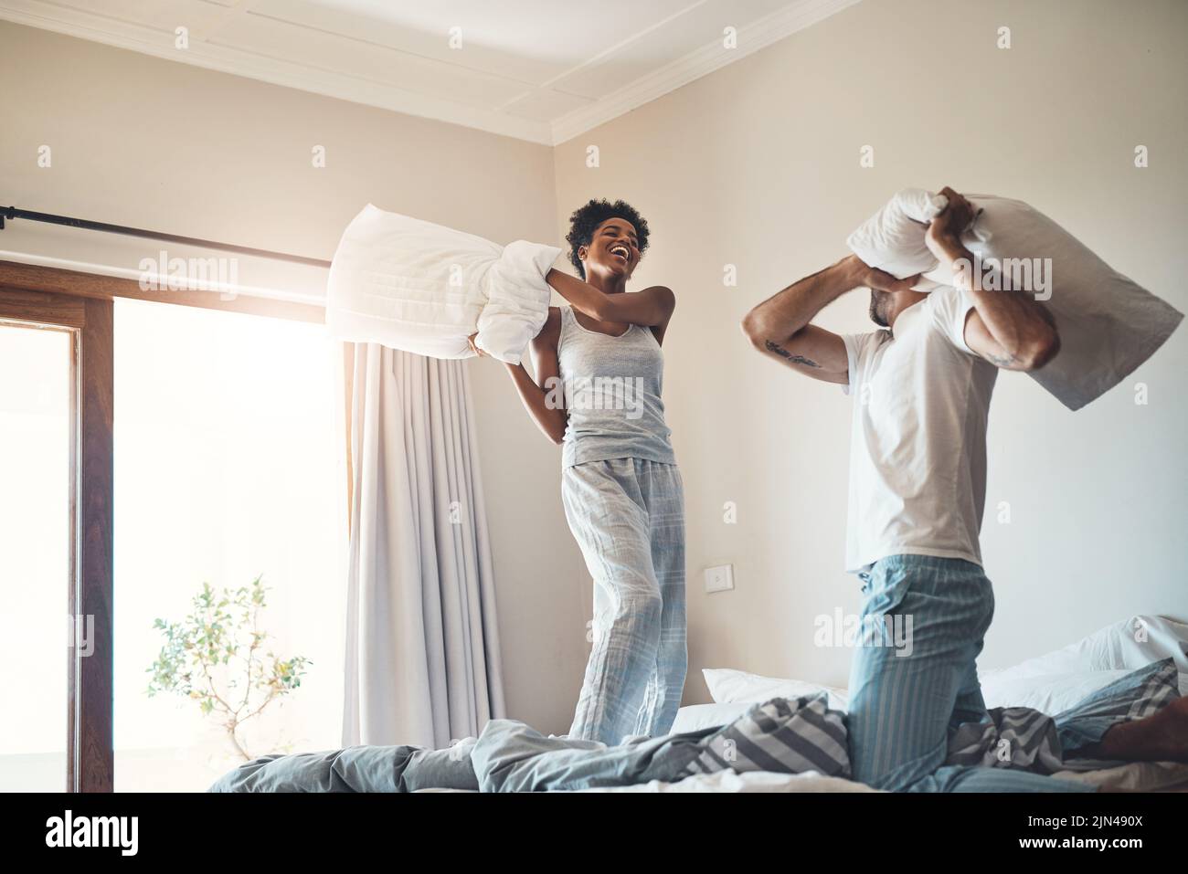 Happy, fun and playful pillow fight of a loving couple playing in their bedroom at home. Funny male and female laughing, smiling and fighting with Stock Photo