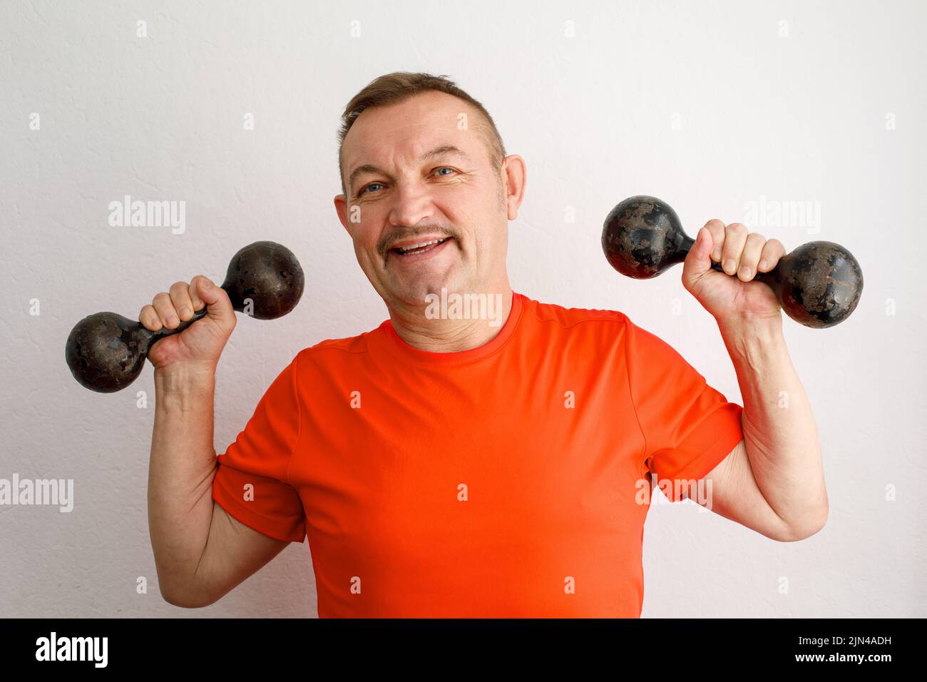 Aged hilarious male lifting dumbbells working out in a home Stock Photo