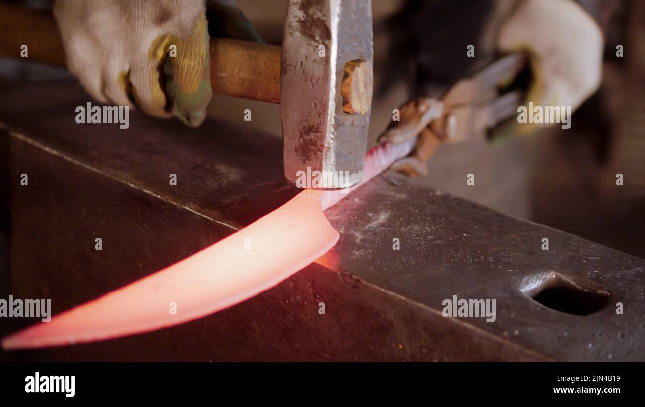 A man blacksmith hitting a hot knife blade with a hammer Stock Photo