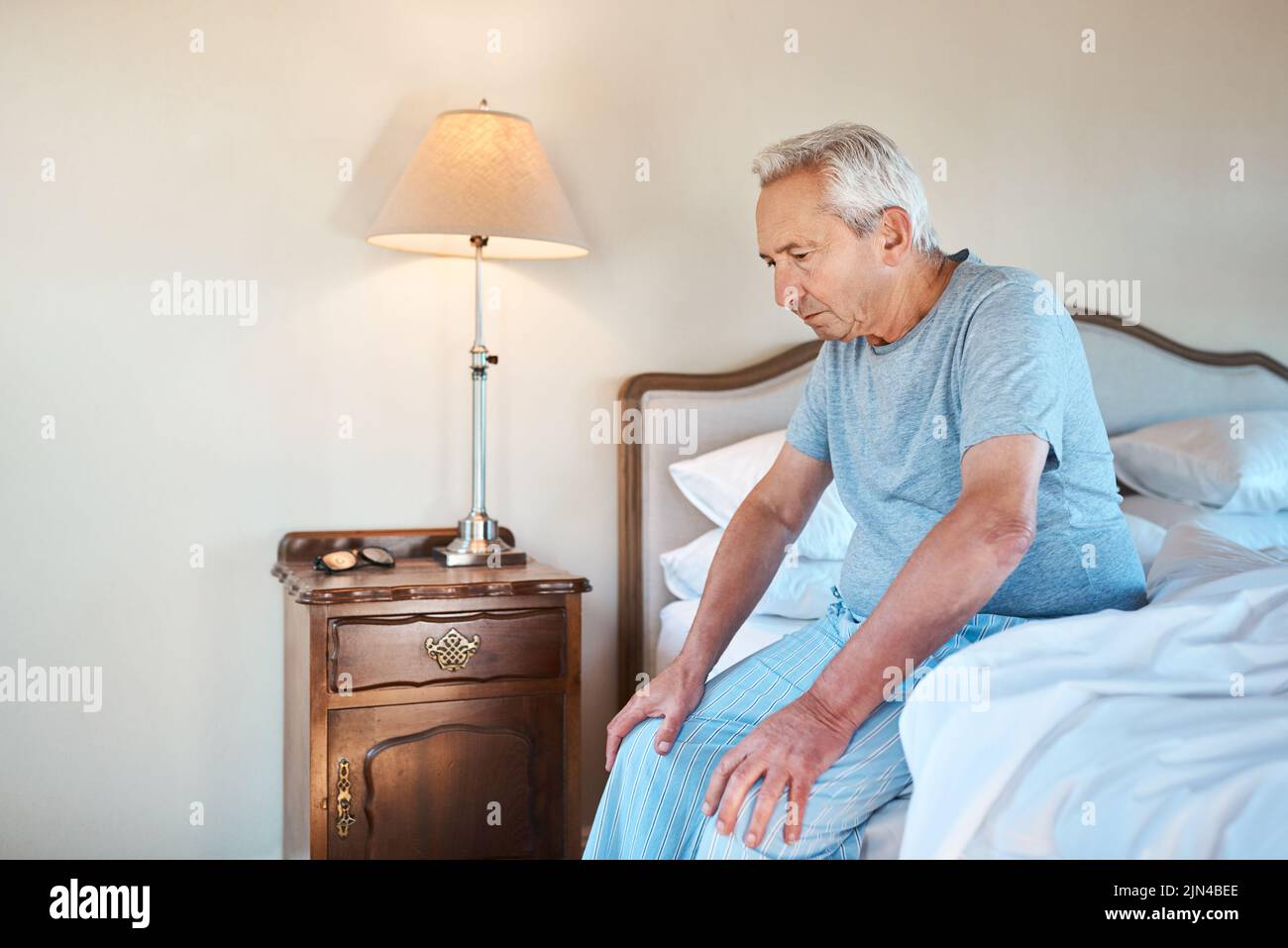 Thinking of how to spend my day. a senior man sitting alone on the edge of his bed and looking contemplative at home. Stock Photo