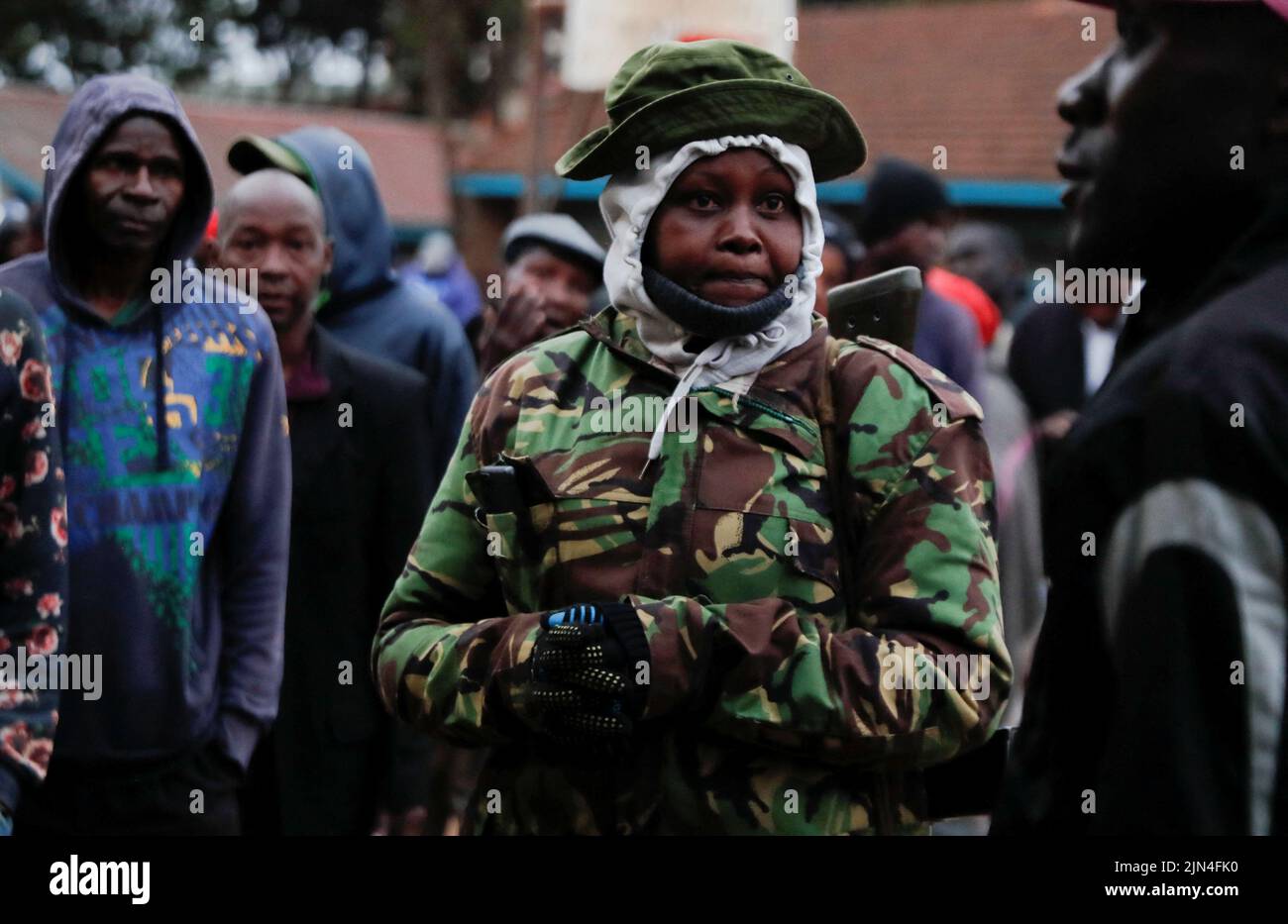 A police officer stands guard as voters queue before casting their ballots during the general election by the Independent Electoral and Boundaries Commission (IEBC) at the Kibera primary school in Nairobi, Kenya August 9, 2022. REUTERS/Thomas Mukoya Stock Photo