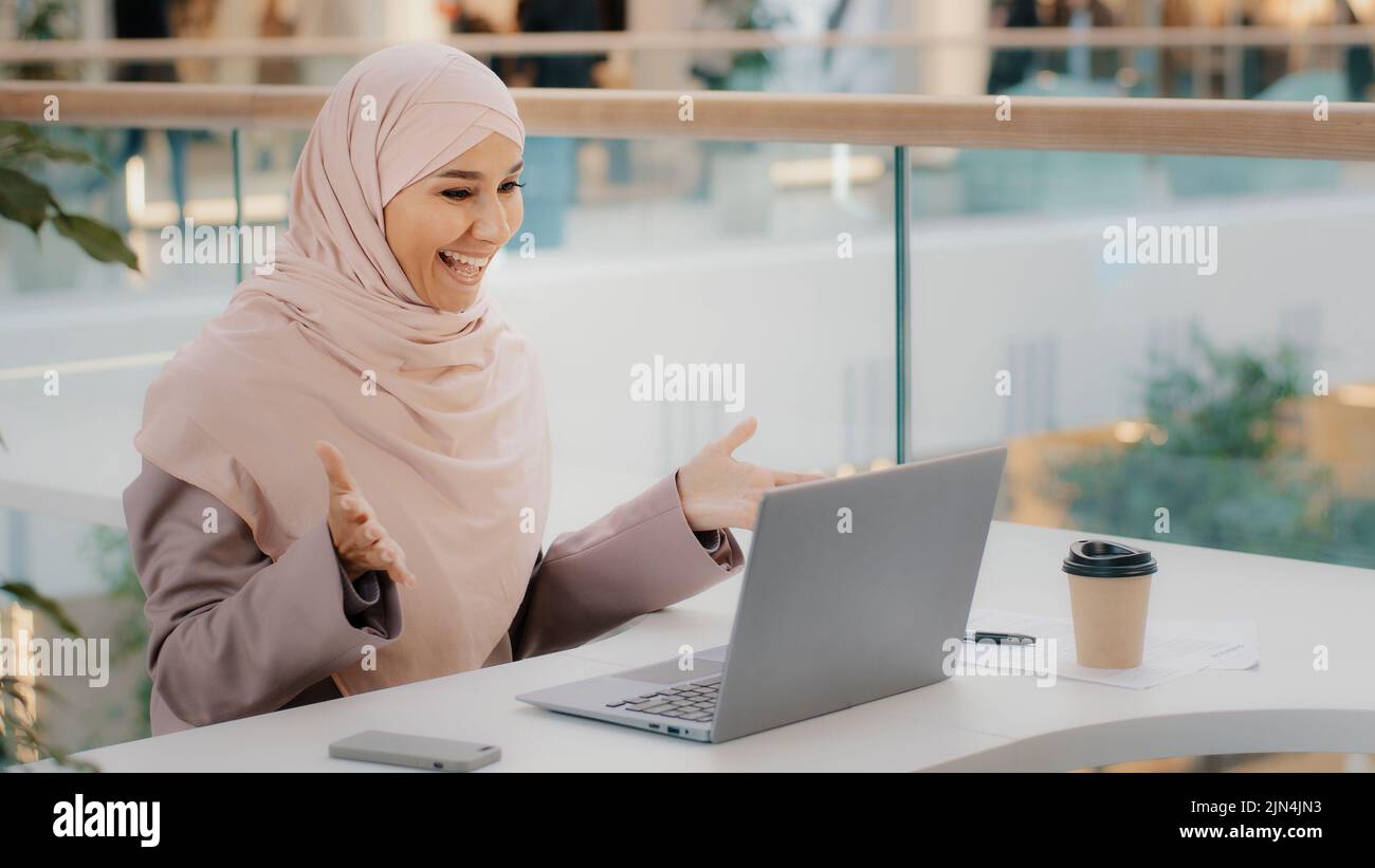 Happy young arab businesswoman sitting at office desk typing on laptop ...
