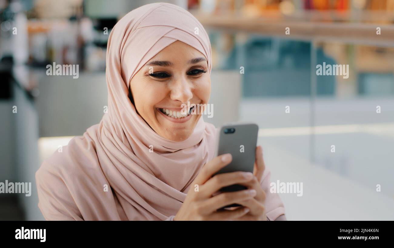 Happy young muslim woman in hijab holding smartphone playing on phone ...