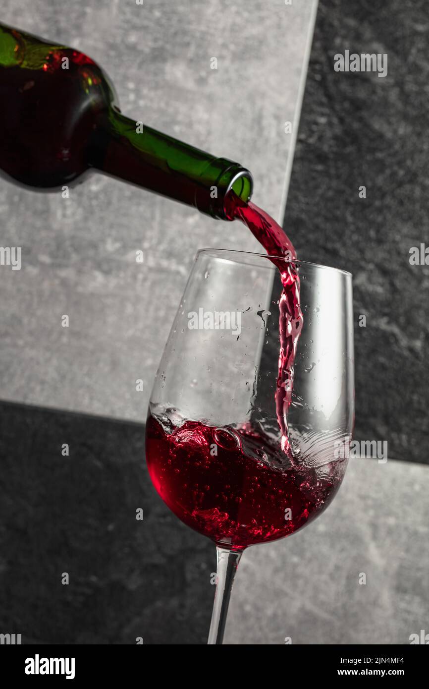 Red wine is poured from the bottle into a glass. Grey and black stone
