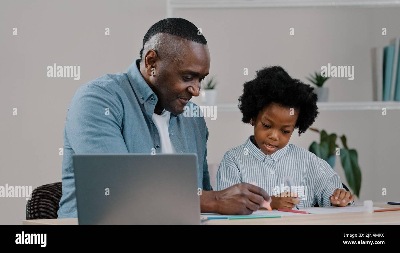 Adult father home teacher helping little daughter to do homework sit at desk in room study remote using laptop man explaining kid girl task african Stock Photo