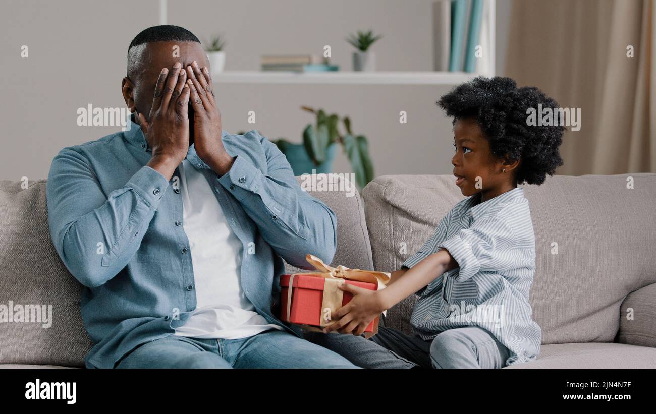 Little loving cute daughter congratulates dad on birthday gives gift adult man closes eyes in anticipation of surprise surprised amazed enjoys express Stock Photo