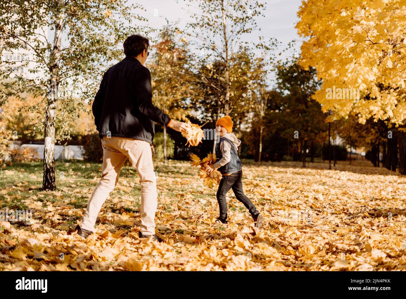 Father and son having fun in autumn park with fallen leaves, throwing