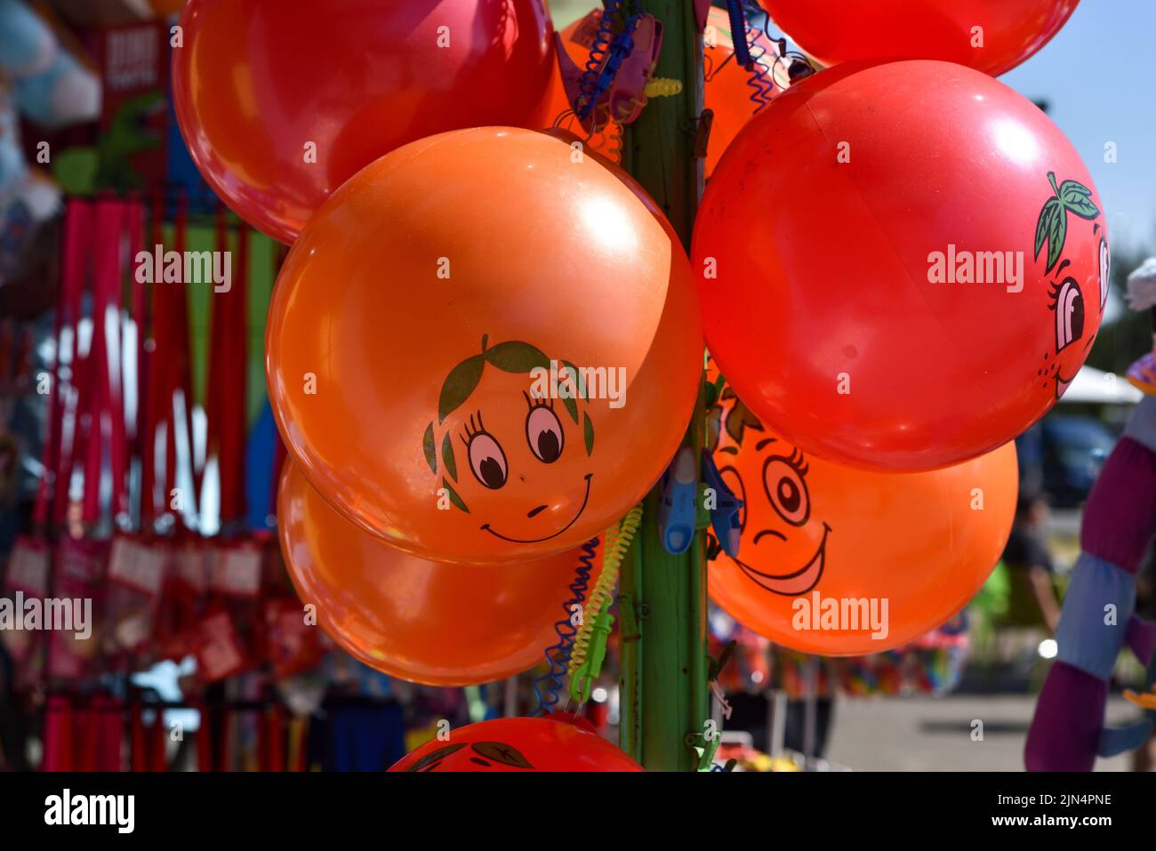 Bright red and orange balloons with smiling faces hanging up for sale at the seaside. Stock Photo