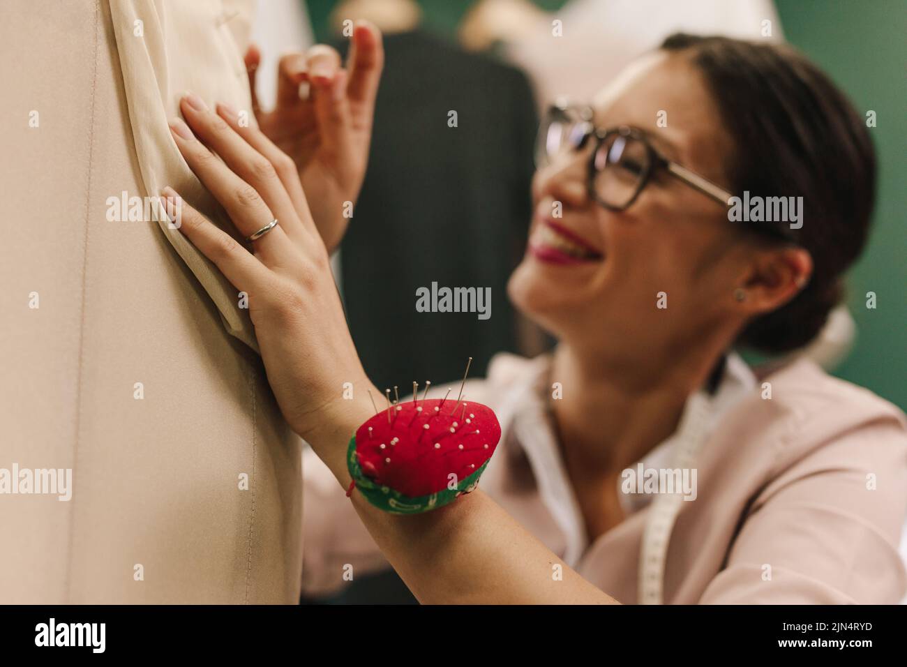 Young asian female dressmaker attaching needles on mannequin. Focus on hands of female designer working on new dress design. Stock Photo