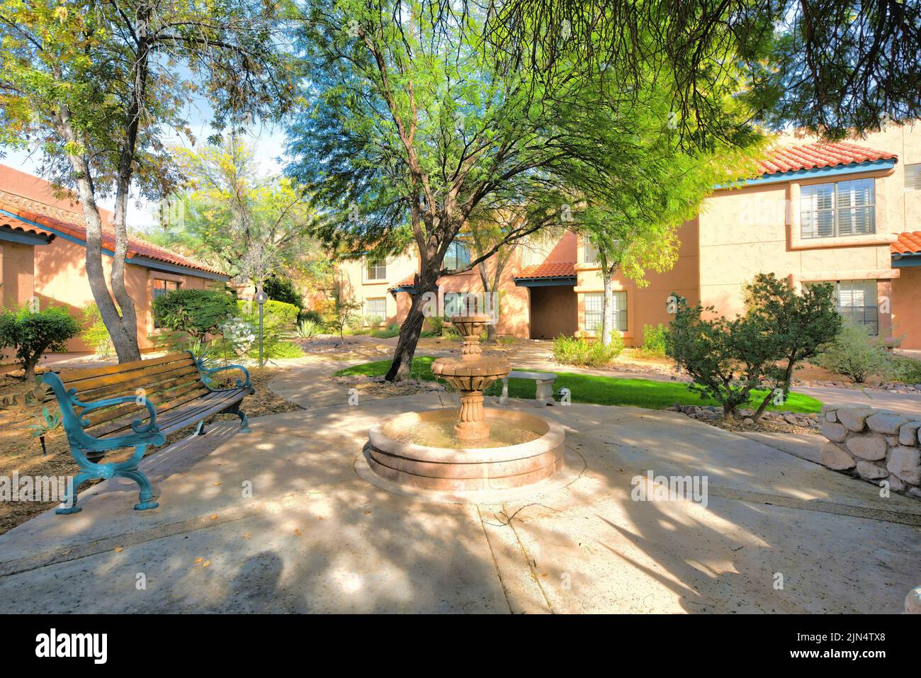 Wooden bench and fountain near the italianate houses in a subdivision at Tucson, Arizona. There are trees and lawn near the walkway leading to the ent Stock Photo