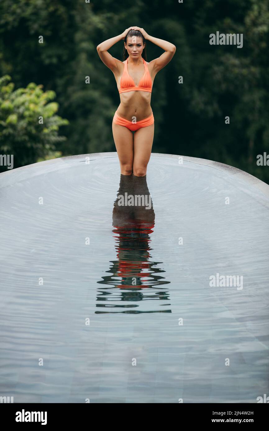 Young beautiful woman standing in water of swimming pool. Sensual woman in bikini posing outdoor. Stock Photo