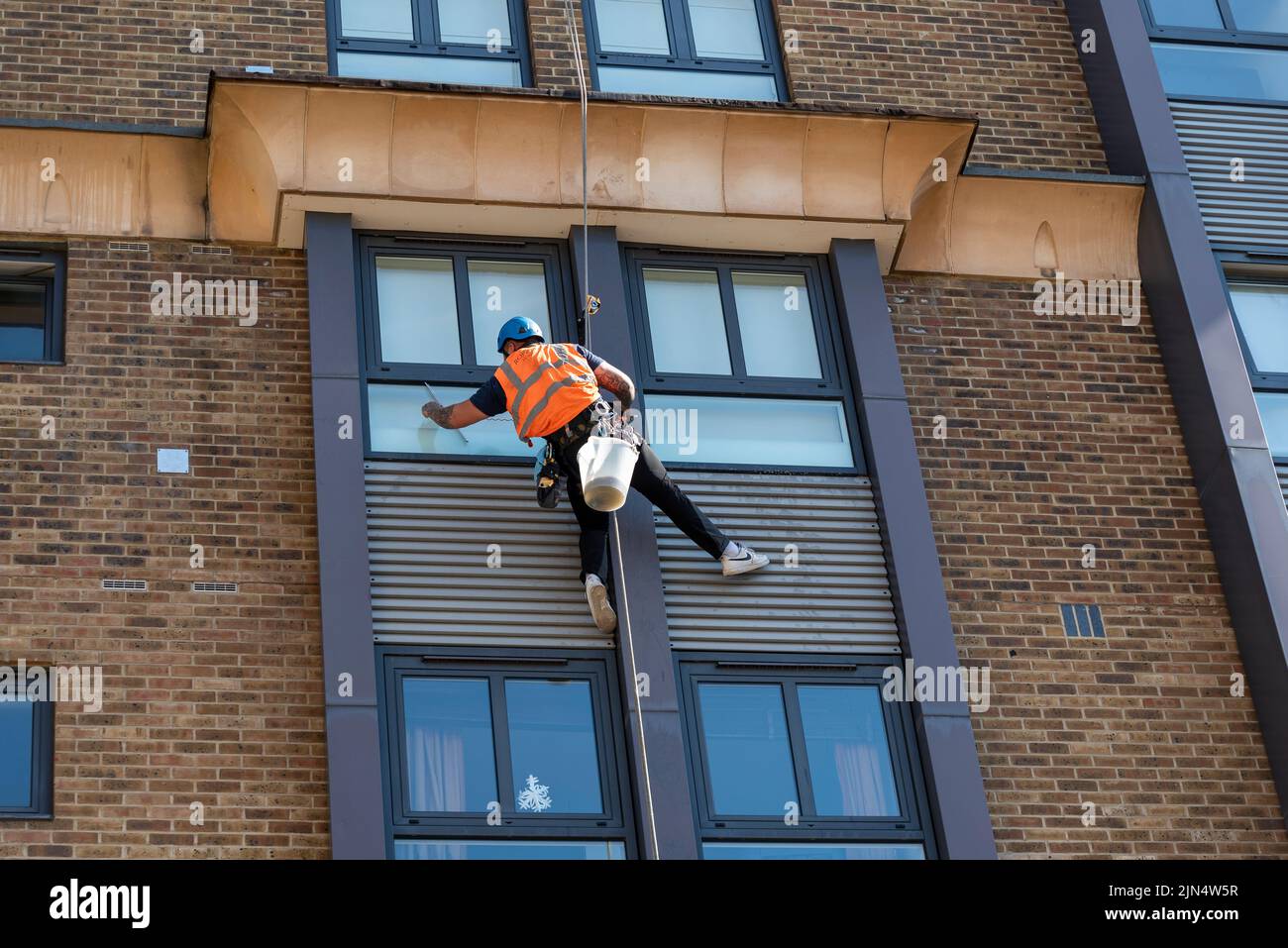 A rope access window cleaner using high rope to clean the windows of a high building in Shad Thames, London, UK Stock Photo