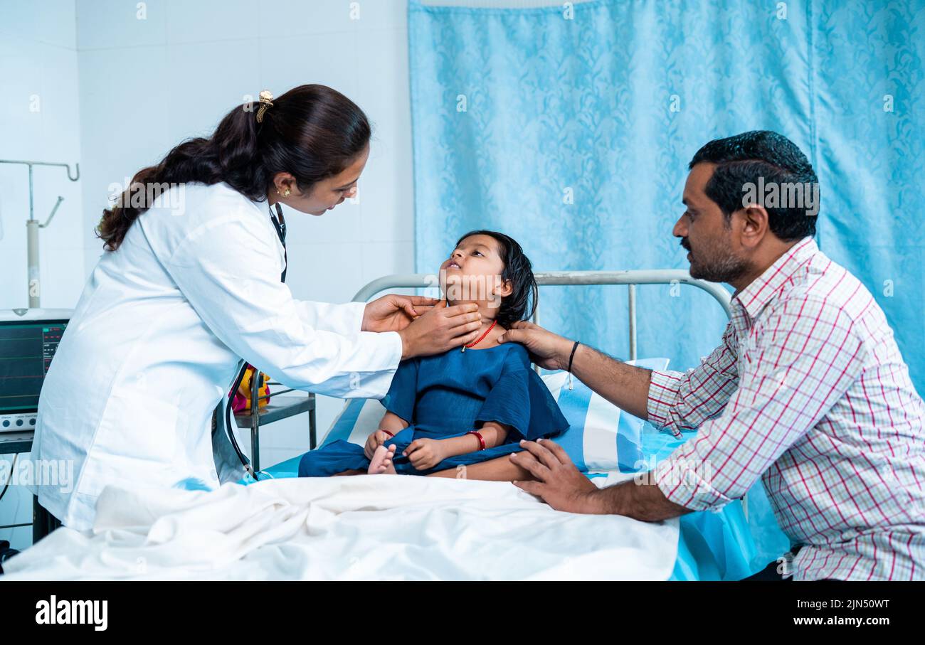 Doctror examining throat infection of girl child at hospital while with father - concept of thyroid problem, medicare and inflammation. Stock Photo