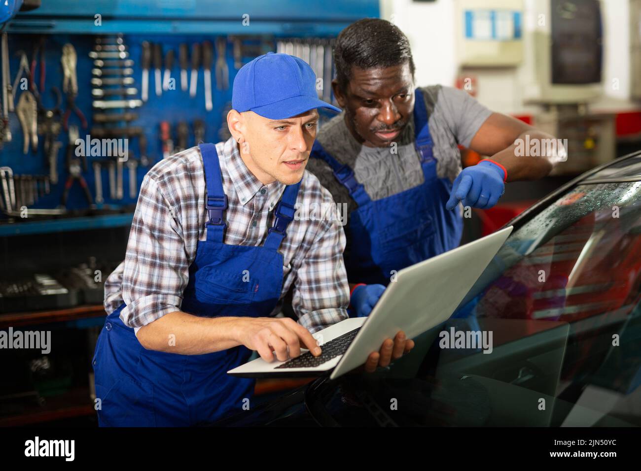 Two auto mechanics diagnosing car engine with laptop Stock Photo