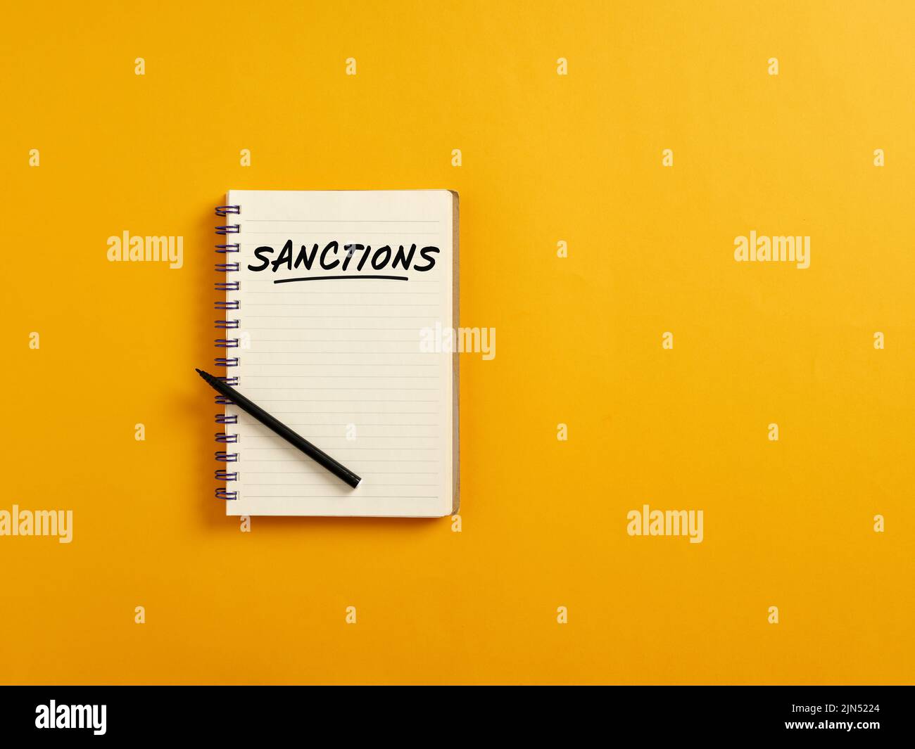 Notepad and black pen on yellow background with the word sanctions. Political or economic sanctions or punishment concept. Stock Photo