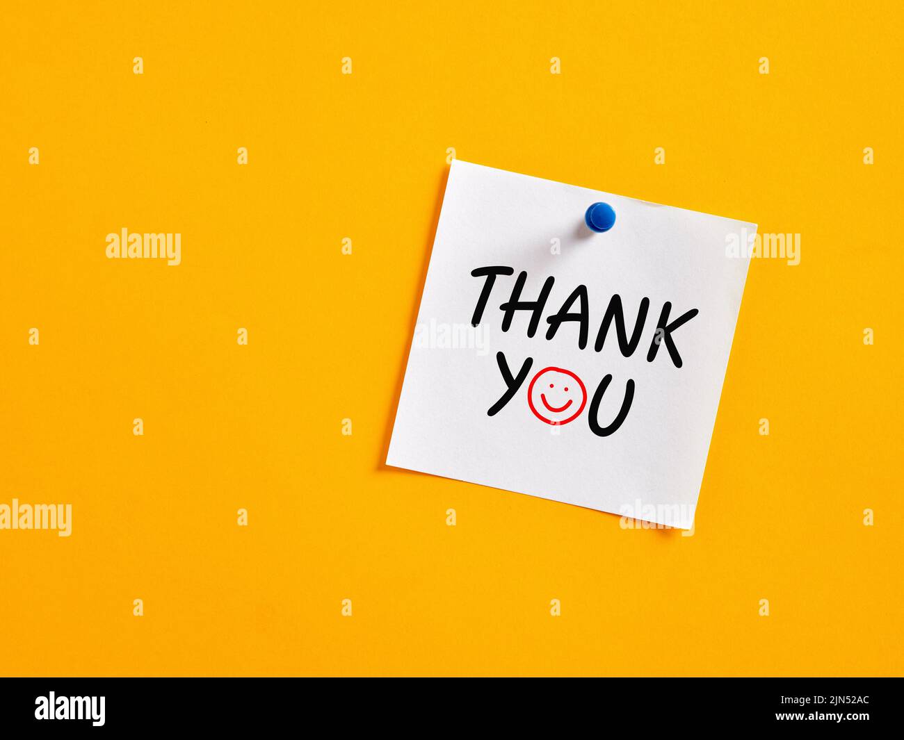 The word thank you written on a note paper pinned on a yellow board ...