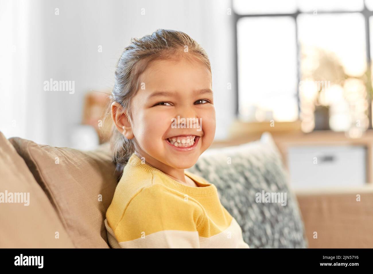 happy smiling little girl sitting on sofa at home Stock Photo - Alamy