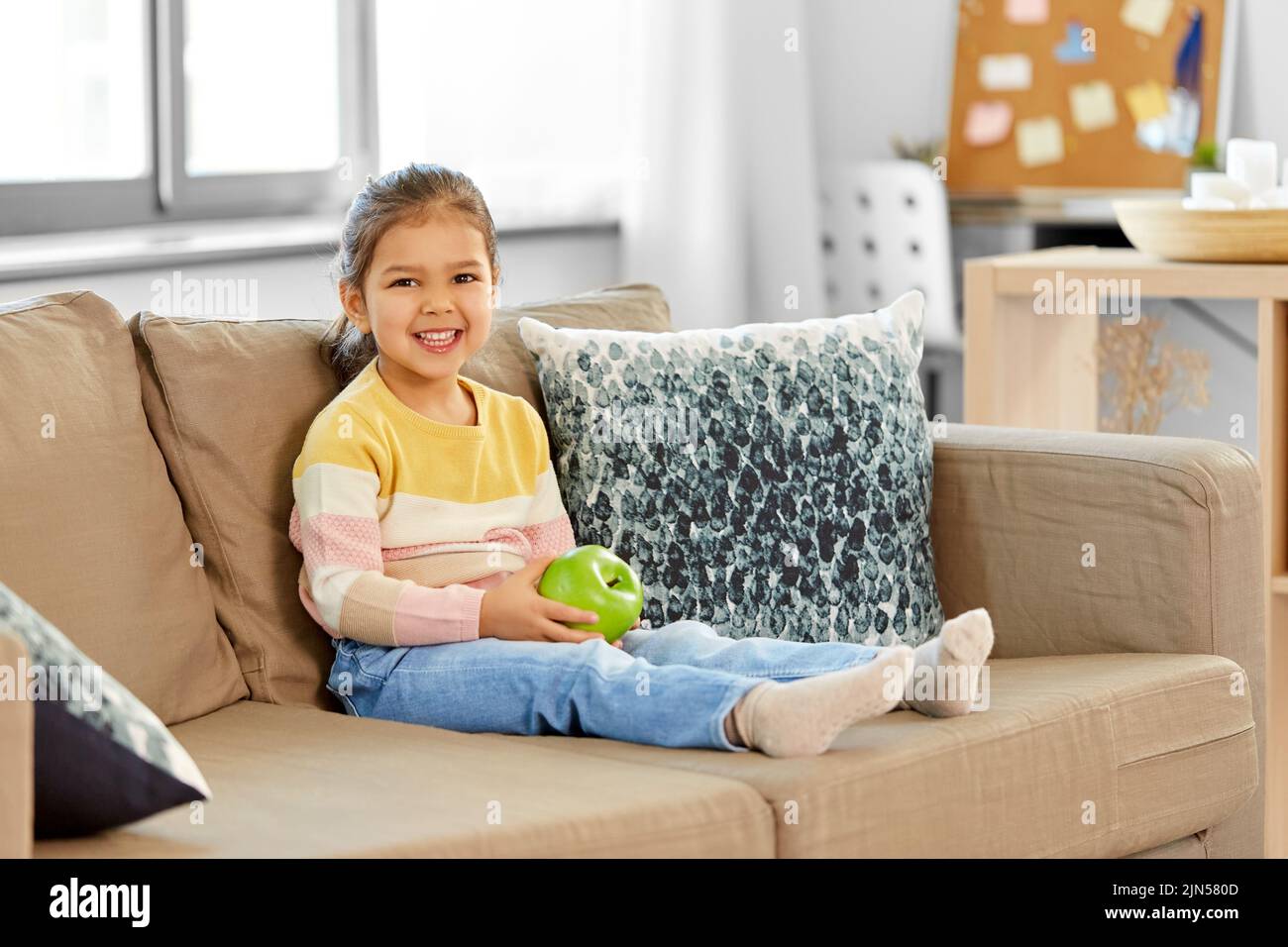 happy little girl with apple sitting on sofa Stock Photo - Alamy
