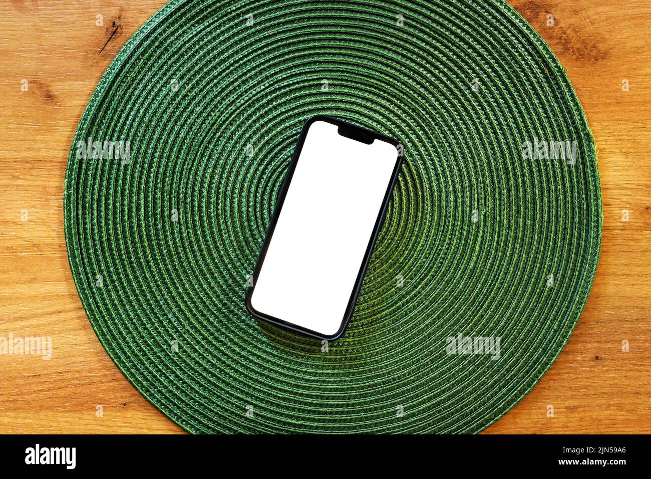 Smartphone with blank mockup touch screen on green plastic table mat, top view Stock Photo